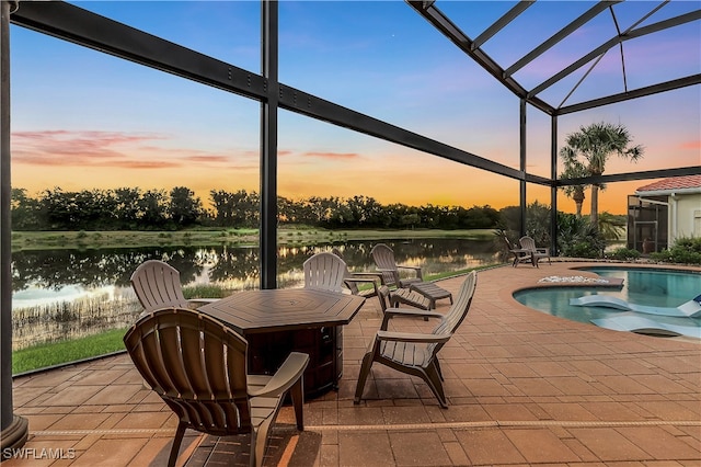 pool at dusk featuring a lanai, a patio area, and a water view