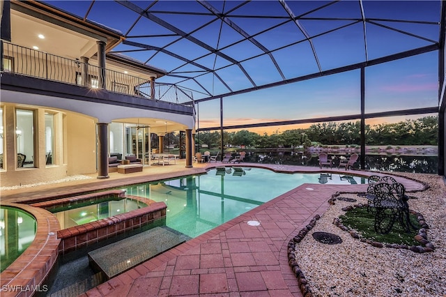 pool at dusk with glass enclosure, an in ground hot tub, a patio, and an outdoor hangout area