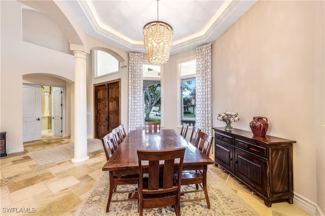 dining area with ornate columns, a notable chandelier, crown molding, a towering ceiling, and a tray ceiling