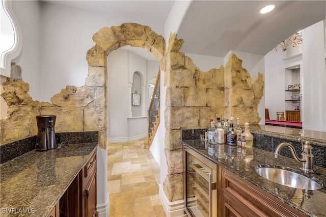 kitchen featuring lofted ceiling, wine cooler, dark stone countertops, and sink