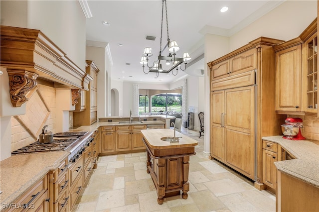 kitchen featuring stainless steel gas stovetop, sink, crown molding, a kitchen island, and a chandelier