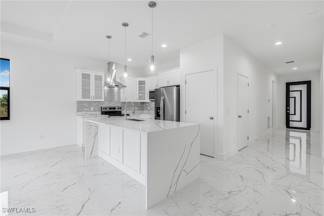 kitchen featuring wall chimney exhaust hood, stainless steel appliances, a center island with sink, white cabinets, and hanging light fixtures