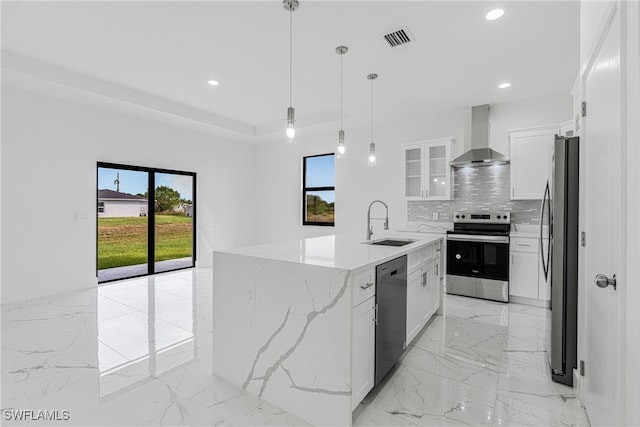 kitchen featuring white cabinets, appliances with stainless steel finishes, a center island with sink, and wall chimney range hood