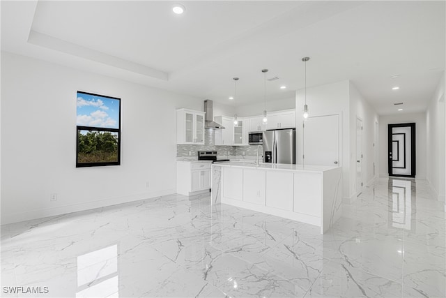 kitchen with hanging light fixtures, stainless steel appliances, wall chimney range hood, a kitchen island, and white cabinets