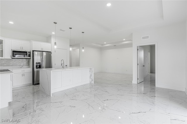 kitchen with backsplash, a kitchen island with sink, white cabinets, hanging light fixtures, and stainless steel appliances