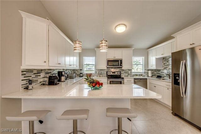 kitchen featuring pendant lighting, white cabinets, tasteful backsplash, a kitchen bar, and stainless steel appliances