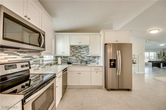 kitchen featuring decorative backsplash, appliances with stainless steel finishes, sink, white cabinetry, and lofted ceiling