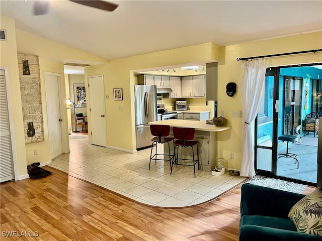 kitchen featuring stainless steel appliances, a kitchen breakfast bar, kitchen peninsula, lofted ceiling, and light wood-type flooring