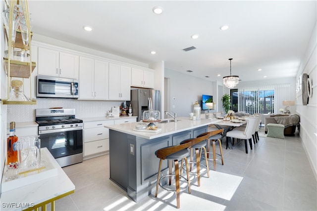 kitchen featuring white cabinetry, a center island with sink, stainless steel appliances, and decorative light fixtures