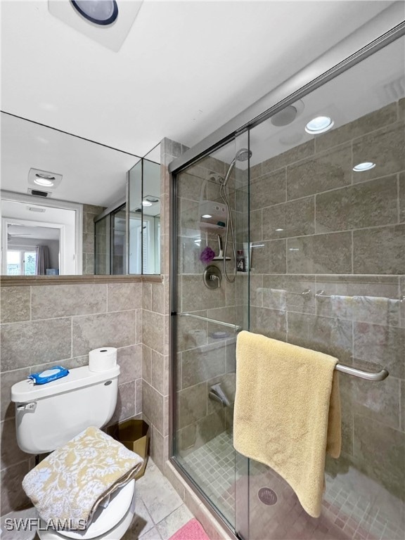 bathroom featuring tile patterned flooring, toilet, tile walls, and a shower with shower door