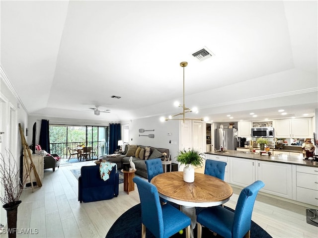 dining space with light wood-type flooring, ceiling fan with notable chandelier, a tray ceiling, and ornamental molding