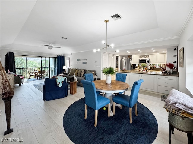 dining area with a tray ceiling, light hardwood / wood-style floors, and ceiling fan with notable chandelier