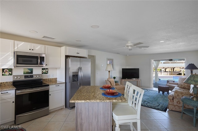 kitchen with white cabinetry, stainless steel appliances, a center island, light stone countertops, and light tile patterned flooring