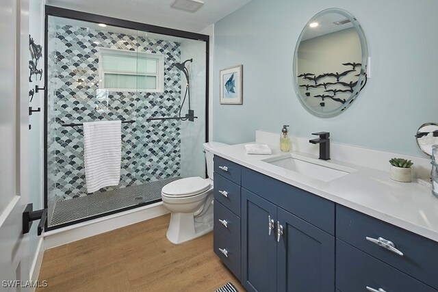 bathroom featuring hardwood / wood-style flooring, vanity, toilet, and a tile shower