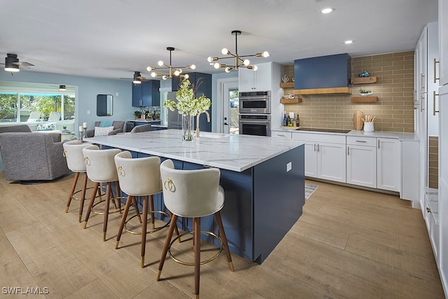 kitchen with tasteful backsplash, double oven, a center island with sink, white cabinets, and hanging light fixtures