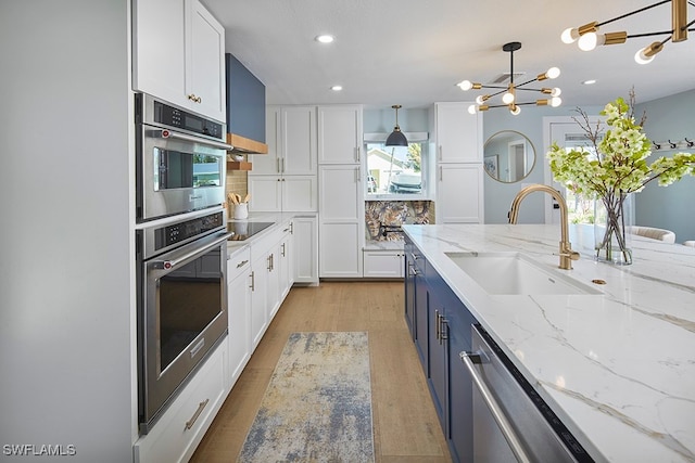 kitchen with white cabinets, decorative light fixtures, light stone counters, and sink