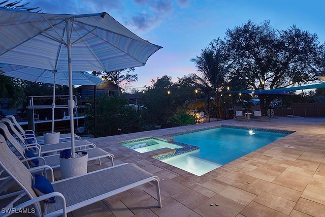 pool at dusk with an in ground hot tub and a patio