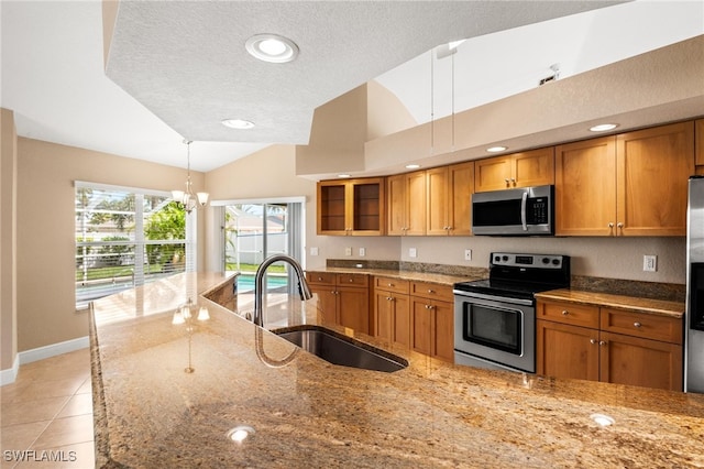 kitchen featuring sink, stainless steel appliances, light stone counters, a textured ceiling, and decorative light fixtures