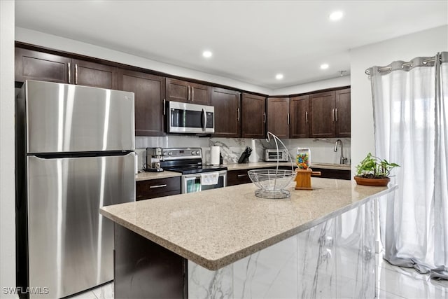 kitchen featuring dark brown cabinetry, light stone countertops, stainless steel appliances, a kitchen breakfast bar, and a kitchen island