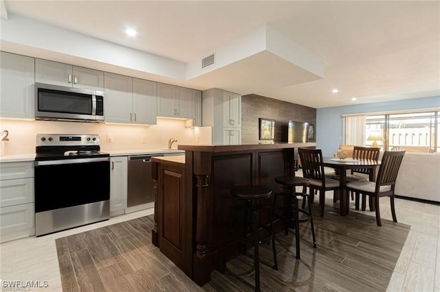 kitchen with gray cabinetry, a breakfast bar, stainless steel appliances, sink, and a kitchen island