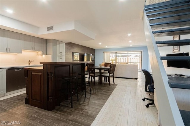 kitchen with sink, stainless steel dishwasher, a breakfast bar, white cabinets, and dark brown cabinets