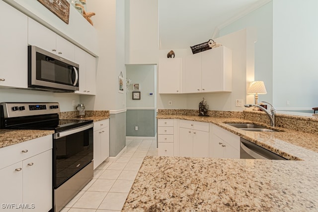 kitchen with light tile patterned floors, stainless steel appliances, a sink, white cabinets, and light stone countertops