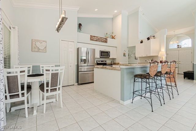 kitchen with stainless steel appliances, a peninsula, a breakfast bar, white cabinetry, and ornamental molding