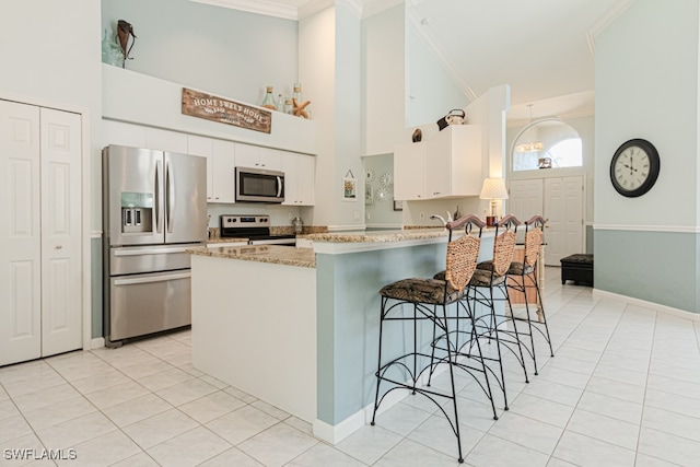 kitchen with light tile patterned floors, light stone counters, stainless steel appliances, white cabinetry, and crown molding