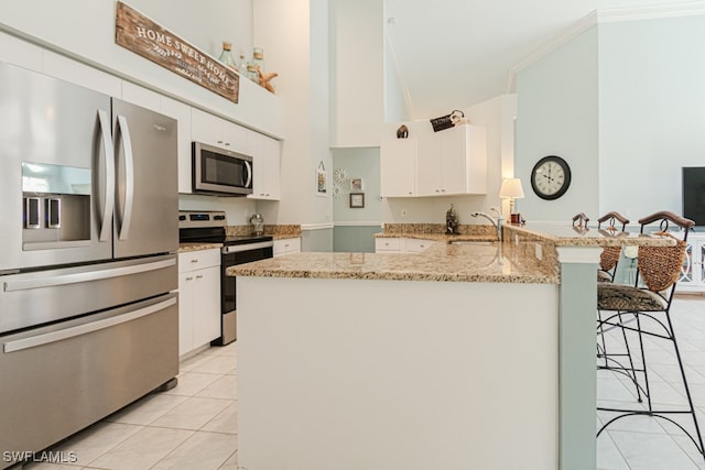 kitchen featuring light stone counters, stainless steel appliances, a peninsula, a breakfast bar, and white cabinets