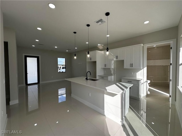 kitchen with stainless steel refrigerator, decorative light fixtures, sink, white cabinets, and a kitchen island with sink