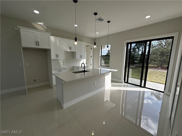 kitchen featuring a kitchen island with sink, sink, light tile patterned floors, decorative light fixtures, and white cabinets