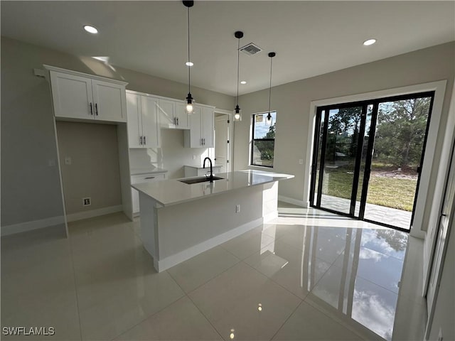 kitchen with light tile patterned flooring, decorative light fixtures, sink, white cabinets, and a center island with sink