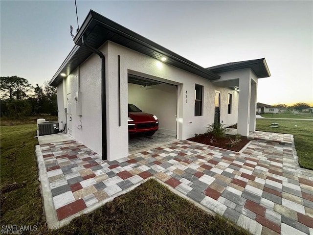 property exterior at dusk featuring central AC, a yard, and a garage