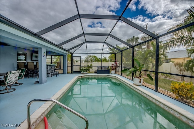 view of pool with exterior bar, a patio, and a lanai