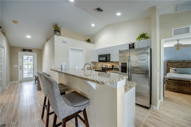 kitchen with light stone counters, stainless steel appliances, light hardwood / wood-style flooring, white cabinets, and a breakfast bar area