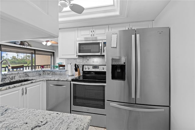 kitchen with sink, tasteful backsplash, light stone counters, white cabinets, and appliances with stainless steel finishes