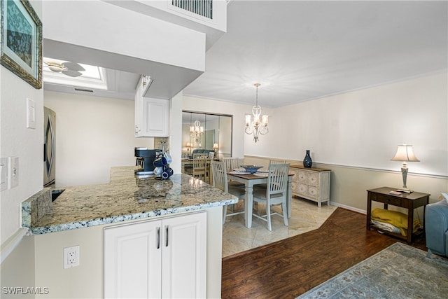 kitchen with stainless steel refrigerator, white cabinetry, light stone counters, pendant lighting, and light wood-type flooring