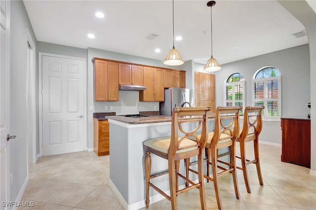 kitchen with light tile patterned floors, decorative light fixtures, a kitchen island, a kitchen bar, and stainless steel refrigerator