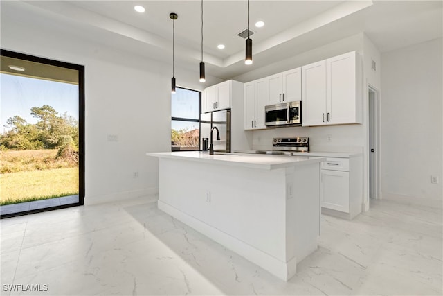 kitchen with a raised ceiling, pendant lighting, a center island with sink, white cabinets, and appliances with stainless steel finishes