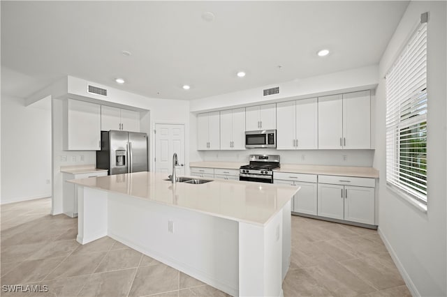 kitchen featuring sink, light tile patterned floors, a kitchen island with sink, white cabinets, and appliances with stainless steel finishes