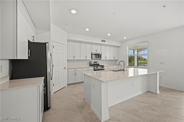 kitchen with appliances with stainless steel finishes, sink, light tile patterned floors, a center island with sink, and white cabinets