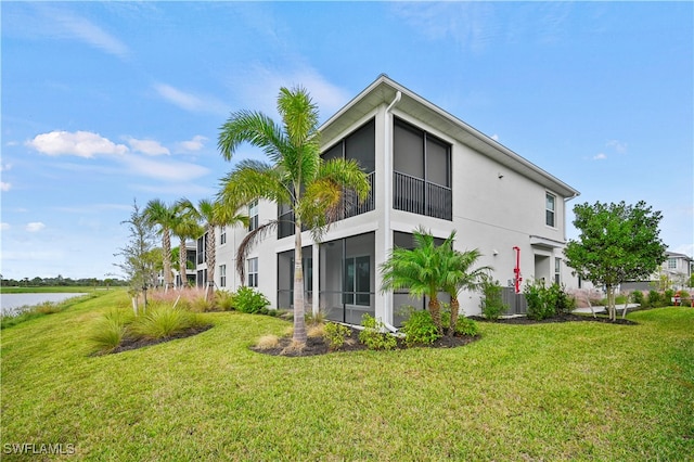 back of house with a sunroom, a water view, and a lawn