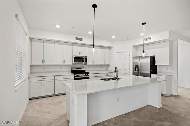 kitchen with appliances with stainless steel finishes, sink, pendant lighting, white cabinetry, and an island with sink