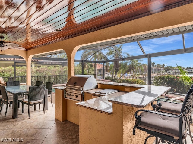 view of patio featuring a lanai, ceiling fan, exterior kitchen, a bar, and a grill