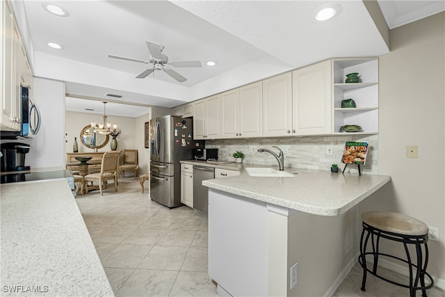 kitchen with kitchen peninsula, backsplash, ceiling fan with notable chandelier, stainless steel appliances, and sink