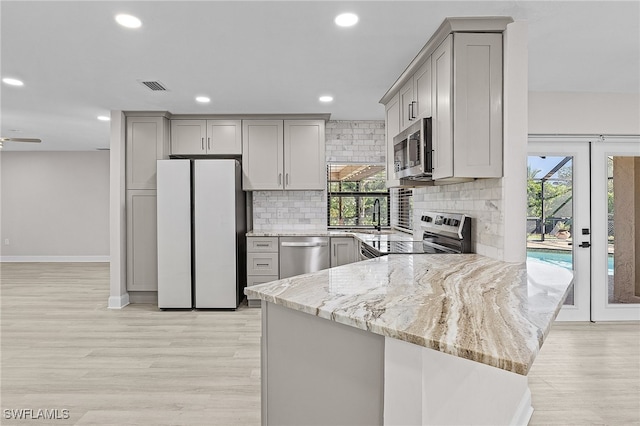 kitchen with gray cabinetry, light stone counters, kitchen peninsula, and stainless steel appliances