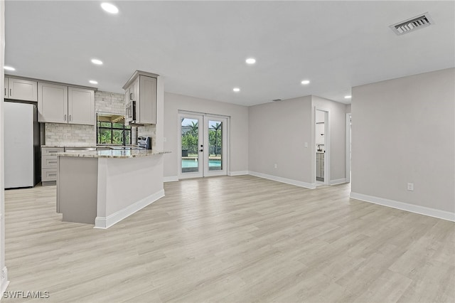 kitchen with gray cabinets, light stone countertops, white fridge, and light hardwood / wood-style floors