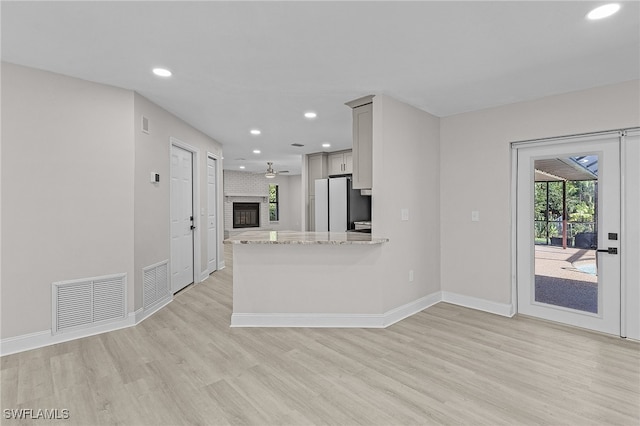 kitchen featuring a brick fireplace, light hardwood / wood-style floors, light stone countertops, white fridge, and kitchen peninsula