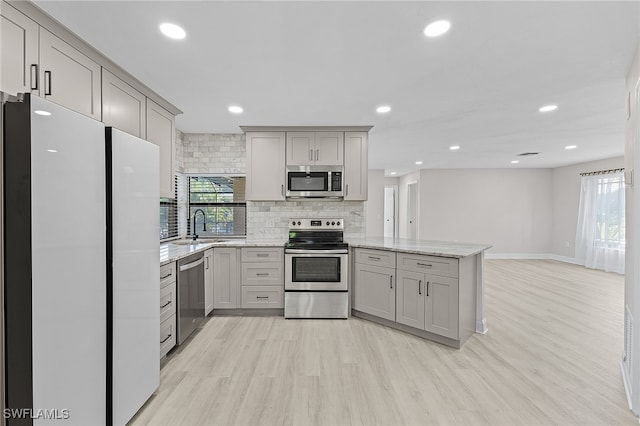 kitchen with gray cabinets, light stone countertops, light hardwood / wood-style floors, and appliances with stainless steel finishes