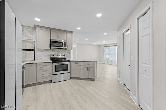 kitchen with backsplash, gray cabinets, stainless steel appliances, and light wood-type flooring